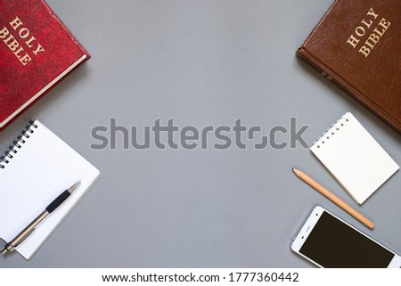 Top view of Holy Bible, notebooks, and smartphone on grey background