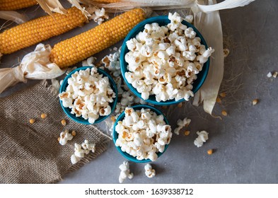 Top view of Home made fresh popped popcorn with unpopped kernels and organic grown dry corn cob against grey background . Copy space 
