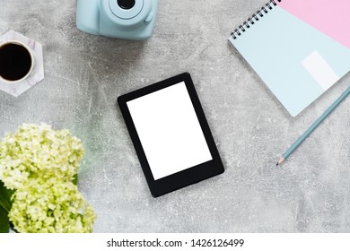 Top view home office desk with feminine accessories and devices. Flat lay e book reader with blank white screen, paper notepad, instant film camera, coffee cup and flowers on concrete surface.  - Shutterstock ID 1426126499