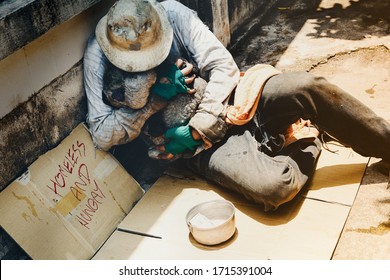 Top view homeless, dirty beggars are all alone, beside the old wall, sitting on cardboard, hugging their daughter's old teddy bear in the midst of the hot afternoon sun.

