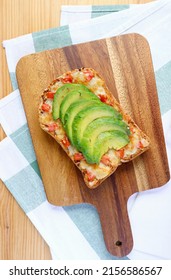 Top view of homemade grilled cheese toast with sliced avocado and tomato on wooden breadboard