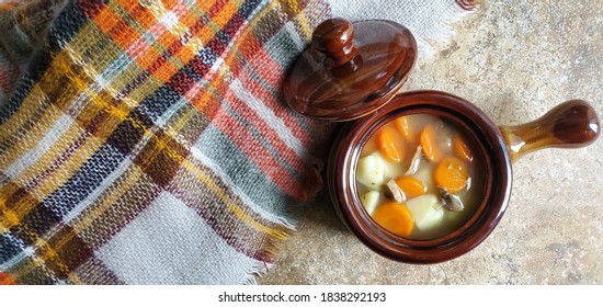 A Top View Of A Hot Bowl Of Chicken Vegetable Soup With A Warm Cozy Oversized Scarf Lying Next To It