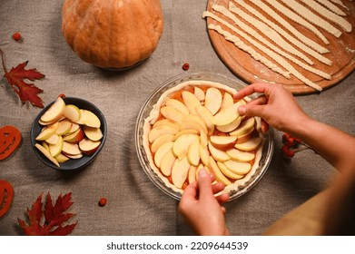 Top view of housewife, chef confectioner putting slices of apples on a raw pumpkin pie, preparing homemade traditional American classic tarte with crust lattice, for Thanksgiving Day. Autumn holidays - Powered by Shutterstock