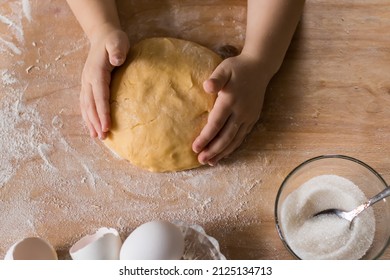 Top view of human children's hands kneading dough on a wooden table in the kitchen. A child helping his mother to cook a pie kneading the dough in the kitchen.