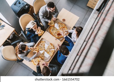 Top View Of Hungry Colleagues Sitting At Table And Having Pizza For Lunch. Corporate Firm Interior.