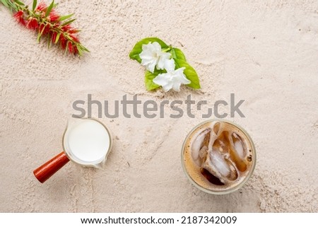 Top view iced coffee, milk and flowers on sand background.
