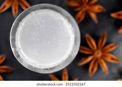 Top view of iced ouzo served in an ice shot glass isolated on a black slate plate among star anise fruits, close-up of an anise-based distilled spirit with louche effect