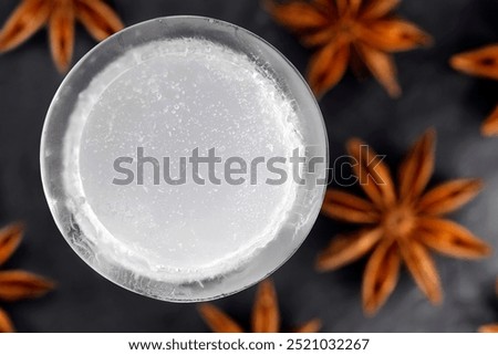 Top view of iced ouzo served in an ice shot glass isolated on a black slate plate among star anise fruits, close-up of an anise-based distilled spirit with louche effect