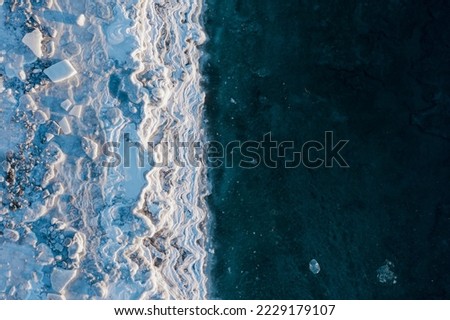 Top view of the icy seashore. Winter aerial photograph of the sea coast. Ice floes and freezing sea water. Nature of the Extreme North. Cold winter weather. Harsh arctic climate. Natural background.