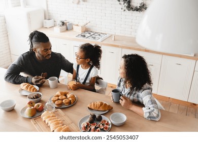 Top view image of African-american family, parents and daughter having morning breakfast at home kitchen, talking and spending time together. Family bonding - Powered by Shutterstock