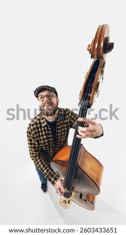 Top view image of bearded double bass player in glasses, smiling while playing, fully immersed in performance against white background. Concept of music, jazz, festival, stage, emotion, energy.