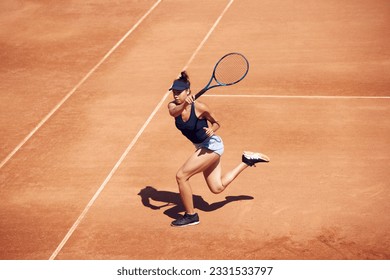 Top view image of competitive young girl, tennis player in motion during game, training at open air tennis court on sunny day. Concept of sport, hobby, active lifestyle, health, strength, ad - Powered by Shutterstock