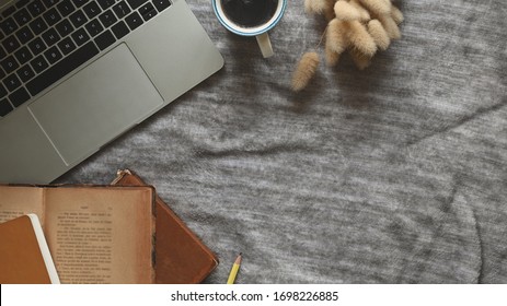Top view image of Computer laptop, Old books, Coffee cup and Wild grass putting together on working table that cover with grey tablecloth as background.