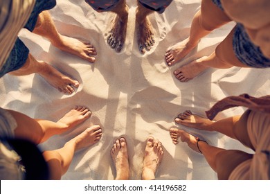 Top view image of feet of young people standing in a circle. Mixed race friends standing barefoot on sandy beach. Concept of unity in diversity.