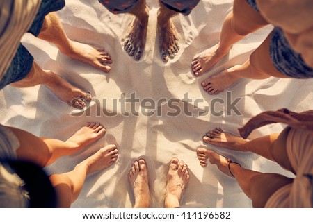 Top view image of feet of young people standing in a circle. Mixed race friends standing barefoot on sandy beach. Concept of unity in diversity.