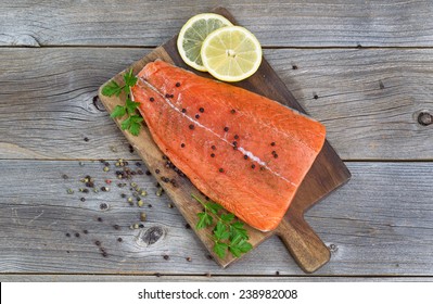 Top view image of a fresh salmon fillet with herbs, spices and lemon slices on rustic wood ready to be cooked. 