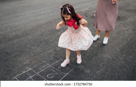 Top View Image Of Happy Little Girl Playing Hopscotch With Her Mother On Playground Outdoors. Child Plays With Her Mom Outside. Kid Plays Hopscotch Drawn On Pavement. Activities And Game For Children