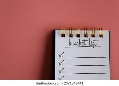 Top view image of notebook with text BUCKET LIST on pink background with copy space. 