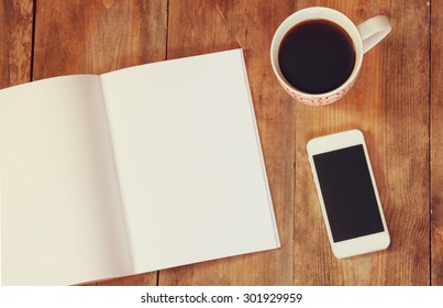 top view image of open notebook with blank pages next to cup of coffee and smartphone on wooden table. ready for adding text or mockup 
