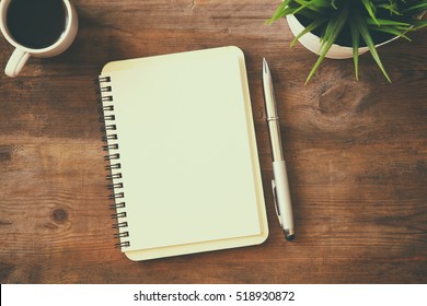 top view image of open notebook with blank pages next to cup of coffee on wooden table. ready for adding text or mockup. Retro filtered