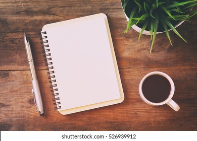top view image of open notebook with blank pages next to cup of coffee on wooden table. ready for adding text or mockup. Retro filtered