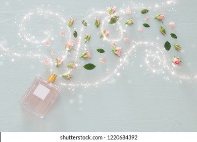 Top view image of perfume bottle with rose petals flowers over pastel blue background. Floral scent concept
