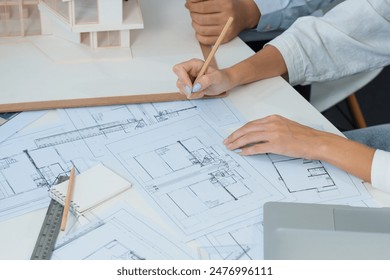 Top view image of professional beautiful young architect hand drafts blueprint while asian cooperative coworker measure house model on table with house model and blueprint scatter around. Immaculate. - Powered by Shutterstock