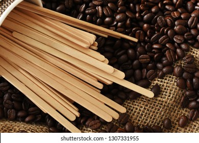 A Top View Image Of Several Wooden Stir Sticks And Roasted Coffee Beans. 