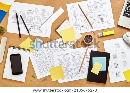 Top view image of web product designers workspace with many website wireframe sketches and sitemap.