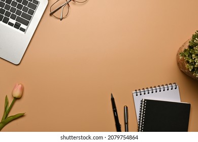 Top view image of a working desk surrounded by a computer laptop, potted plant, notebook, eyeglasses, pens and tulip flower.