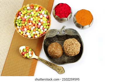 Top view of Indian Makar Sankranti special Sesame seed ball called Till ke laddu in bowl colorful sweet halva in gold bowl and spoon haldi kumkum in silver pot on white background selective focus