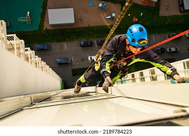 Top View Industrial Mountaineering Worker Hangs Over Residential Facade Building During High Rise Washing Work. Rope Access Laborer Hangs On Wall Of House. Concept Of Industry Urban Works. Copy Space