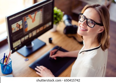 Top view of intelligent blond young woman working with computer and graphic tablet, stylus, smiling. She is a successful self employed retoucher and photograph - Shutterstock ID 650415742