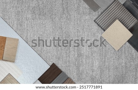 top view of interior material samples board contains ash vinyl flooring tile, stone ceramic tiles, interior fabric wallpapers, wooden laminated flooring placed on grey fabric carpet floor.