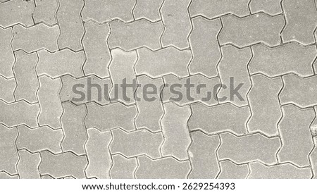 Top view of interlocking concrete pavement blocks in a zigzag pattern. Grey industrial paving stone texture, commonly used in sidewalks, driveways, and public walkways.