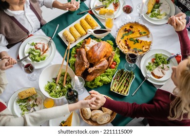 Top View Of Interracial Family Holding Hands While Praying Near Tasty Meal Served For Thanksgiving Celebration