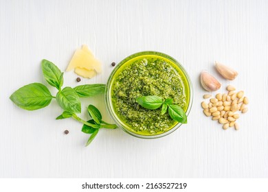 Top view of Italian genovese local herbal pesto sauce made of blended parmesan cheese, green basil leaves, pine nuts, garlic, black pepper and olive oil served in glass bowl on white wooden background