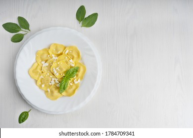 Top view of italian ravioli pasta filled with parmesan cheese decorated by basil leaves in a round plate surrounded by green spinach on white wooden background at kitchen. Image with copy space - Powered by Shutterstock