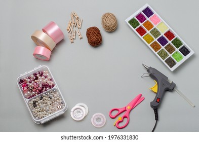 Top View Of Items And Tools For Handmade, Crafts, Needlework: Scissors, Glue Gun, Beads, Beads, Threads, Wooden Clothespins. DIY, Needlework Lessons.Satin Ribbons.On A Gray Background.