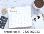 Top view of January 2025 calendar. January 2025 calendar and cup of coffee, calculator, wireless headphones on the table. Happy new year 2025 concept