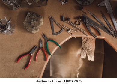 Top View Jewelry Maker Workbench With Tools On Table. Equipment And Tools Of A Goldsmith On Wooden Working Desk Inside A Workshop.