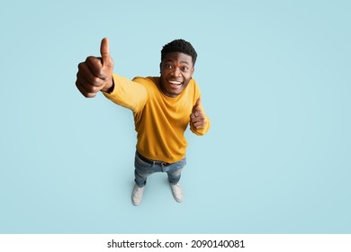 Top view of joyful handsome african american millennial guy in nice outfit showing thumb up and smiling at camera on blue studio background, recommending something exciting, copy space, full length - Shutterstock ID 2090140081