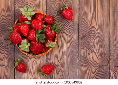 Top view of juicy strawberries in a wicker bowl on a brown shabby rustic wooden table