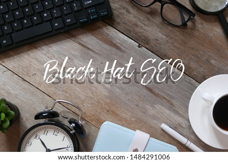 Top view of keyboard, sunglasses,magnifying glass,a cup of coffee, pen, notebook,clock and plant on wooden background written with Black Hat SEO.