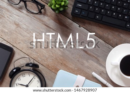 Top view of keyboard,plant,sunglasses, a cup of coffee,pen,notebook,clock and mobile phone on wooden background written with HTML5.