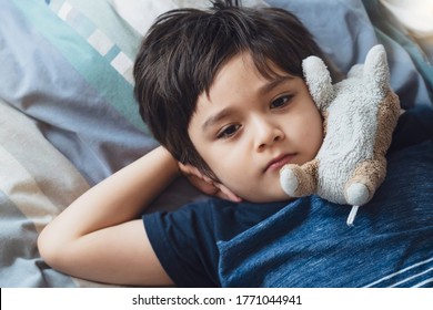 Top view kid lying down on bed and looking up with thinking face, Candid young boy laying down with dog toy on his bed room. Child relaxing on his own in his bed.