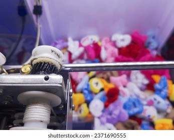 Top view kid play claw machine game in picker arcade inside modern shopping mall. Selective focus on claw, blurred blurry colorful gift plush doll to pick in the background with bokeh light. Retro fun