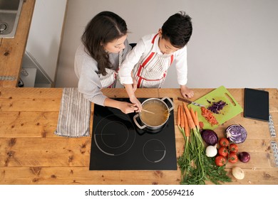 Top View Of The Kitchen: A Single Parent Family Cooking Pasta Together. Mother And Son Stirring Pasta In The Pot. Children Helping Parents. Healthy Eating.