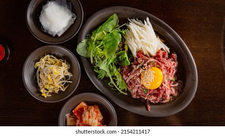 Top view of Korean Grilled BBQ combo sets with egg yolk beef tartare with pickle salad on the dark plate and black table vibe background, and pickle dishes