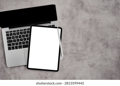 Top view of a laptop computer and a digital tablet with a blank white screen and a stylus pen on a rustic gray textured surface with copy space for text